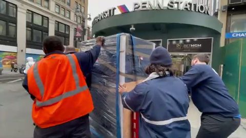 moving crew pushing a shrink-wrapped server rack on a dolly on a city street
