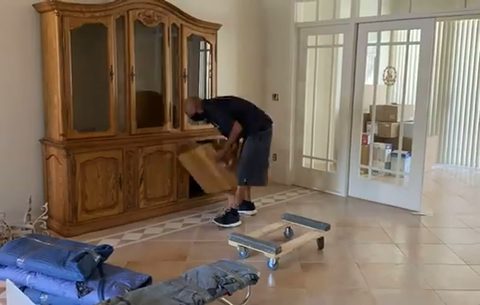 mover fitting cardboard protection on an ornate wood china hutch with furniture dollies ready